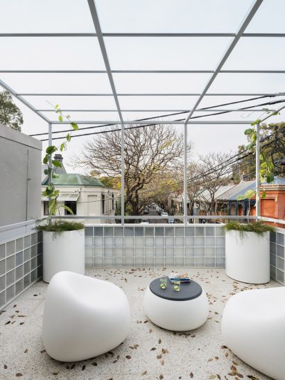 A terrazzo floored terrace with white furniture and a steel overhead structure in The Corner House