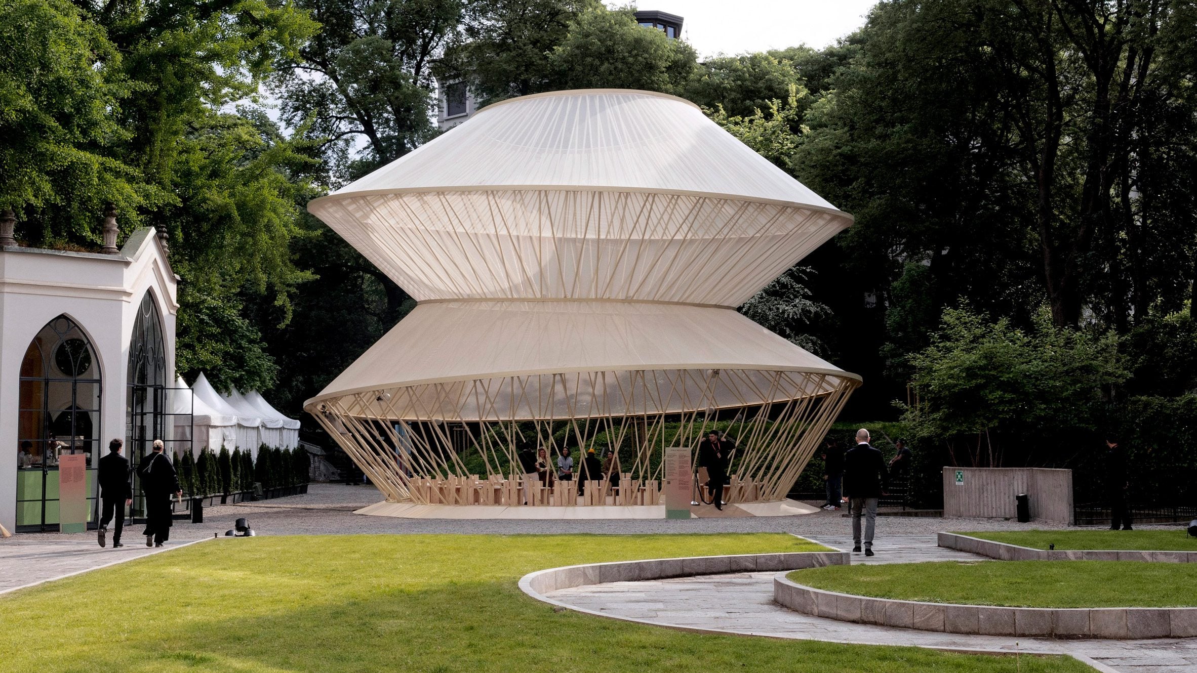 Garden setting with the yurt pavilion surrounded by trees and visitors walking nearby