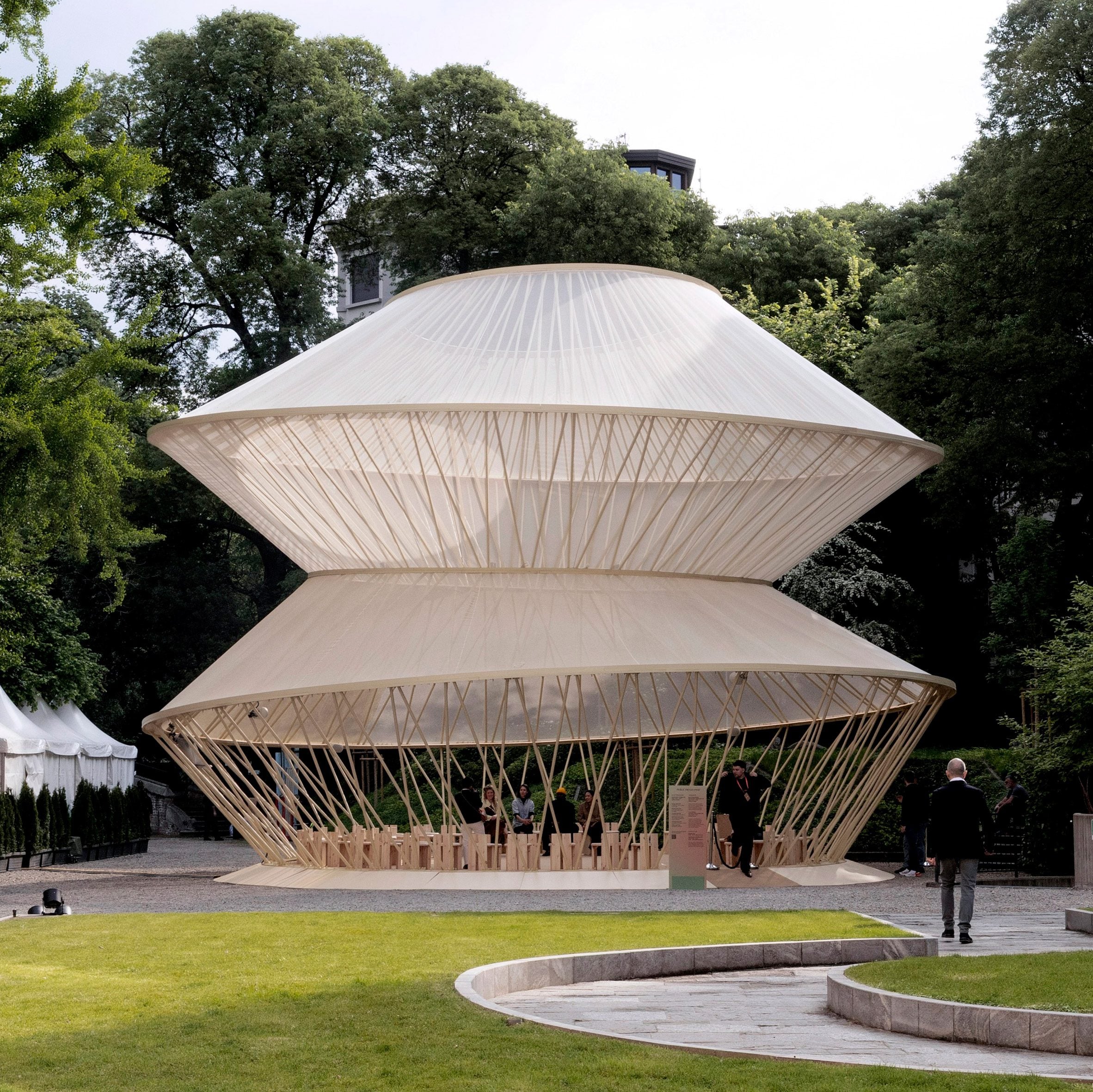 Garden setting with the yurt pavilion surrounded by trees and visitors walking nearby