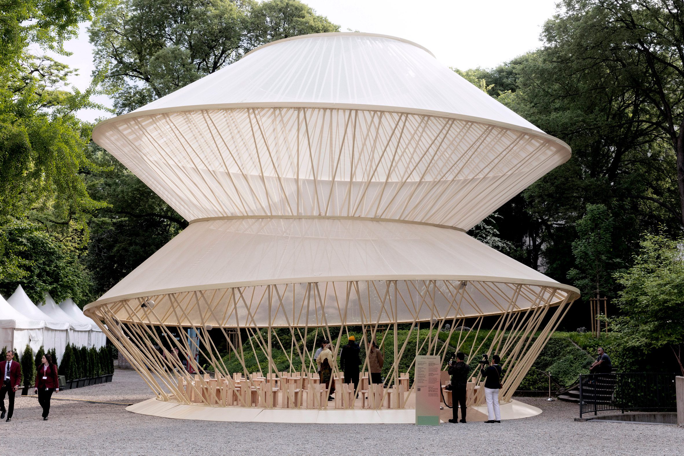 Large circular pavilion with a latticed timber structure and layered canopy set within a garden