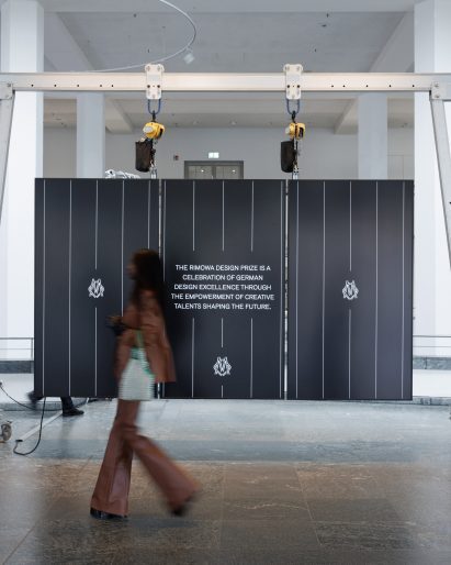 Visitor walking past the Rimowa Design Prize exhibition installation in a large gallery space