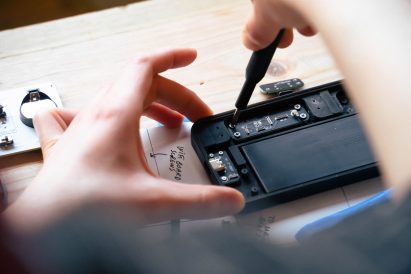 Close-up photo of a person's hand as they use the Repair Kit for Grown-Ups Mobile Phone Edition, screwing a tiny screw