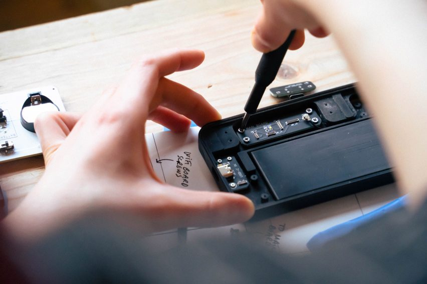 Close-up photo of a person's hand as they use the Repair Kit for Grown-Ups Mobile Phone Edition, screwing a tiny screw