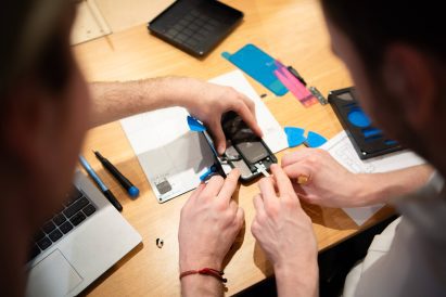 Photo of two pairs of hands as they collaborate on the Repair Kit for Grown-Ups to practice fixing a smartphone