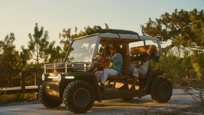 Lifestyle photo of a group of young people driving the Amble One buggy down a coastal path with surf boards strapped to the roof