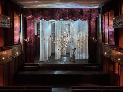 Crystal-like pendant lights suspended in front of translucent white curtains inside theatre