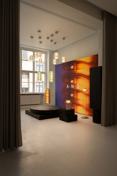 View into a gallery space displaying suspended cylindrical pendant lights