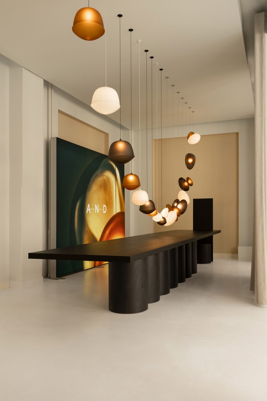 Long black table beneath hanging pendant lights in an exhibition room