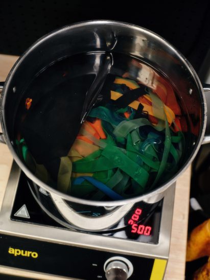 Photo of the Other Matter Leather-making process with strips of coloured plastic film in a big pot of water on a hob