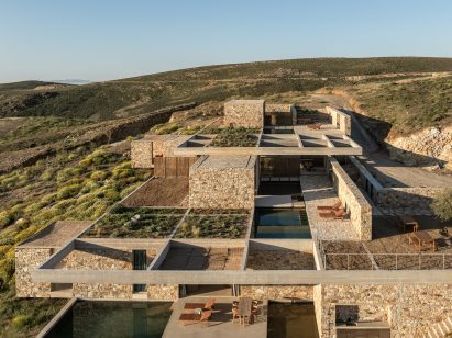 Stone-clad buildings and planted roofs arranged beneath a concrete grid structure
