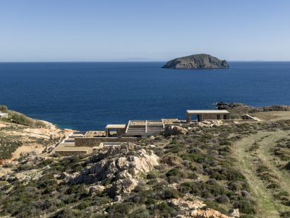 Stone accommodation units embedded into a coastal hillside overlooking the Aegean
