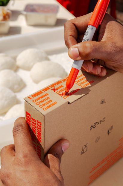 Close-up photo of a person's hands as they fill out a checkbox list on the side of a pizza box with words like empowered, fulfilled and relieved