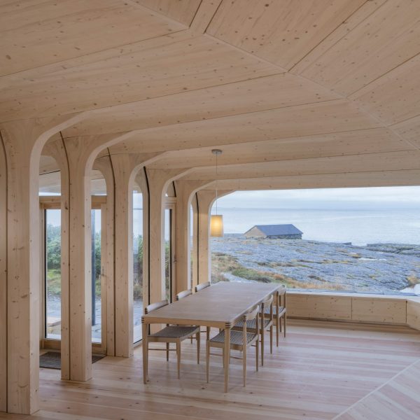 Timber dining space overlooking the rocky coastline through a wide panoramic window