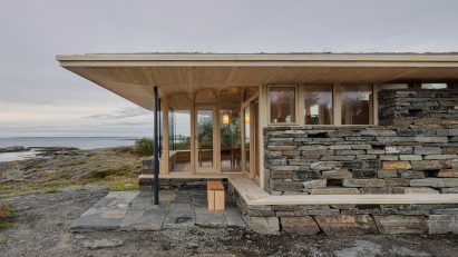 Corner of the timber cabin showing projecting roof, stone plinth and large glazed openings