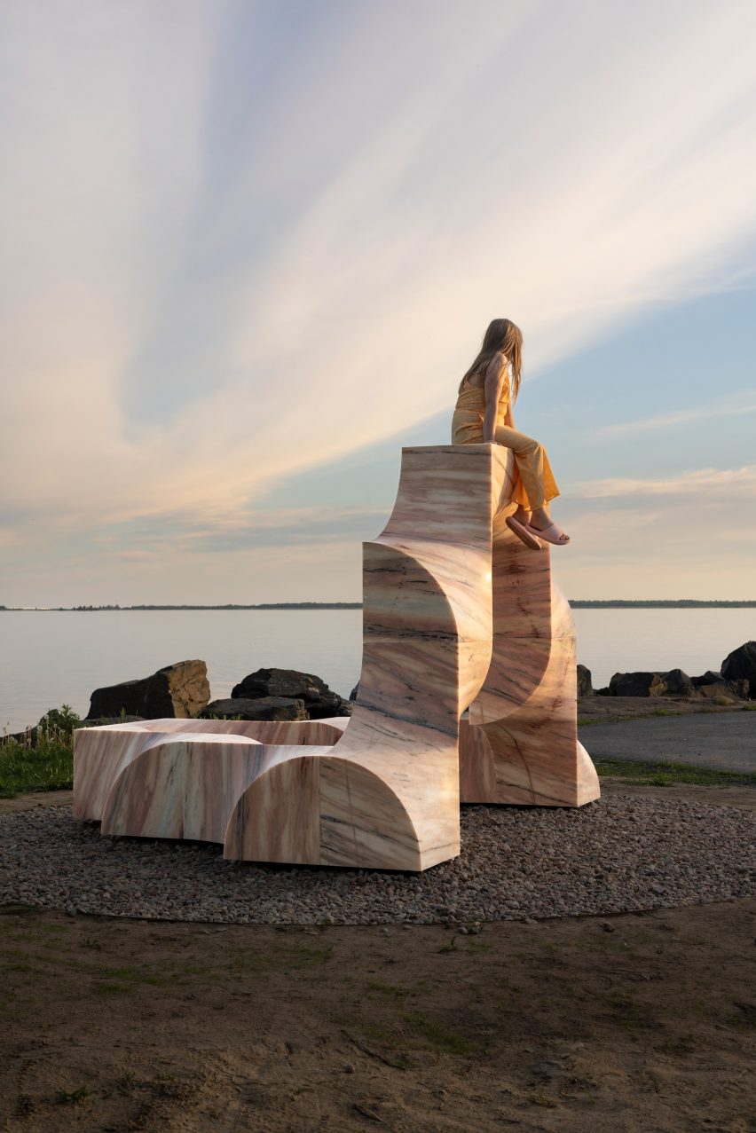 Photo of the Super Kello public art sculpture with pink marble surfaces gleaming in the low sunlight and a girl sitting on top of the arch