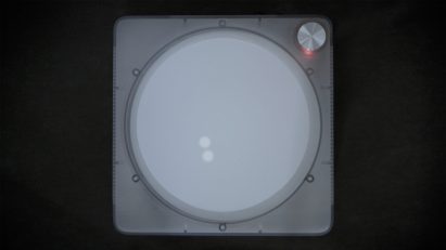 Overhead view photo of the Imago device, showing a record player-like gadget with a simple white circular touchscreen lit up with two glowing dots