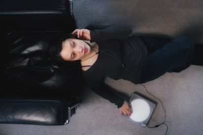 Photo of a woman sitting in repose while wearing headphones, with her fingers resting on a the circular white touchscreen of the Imago audio player