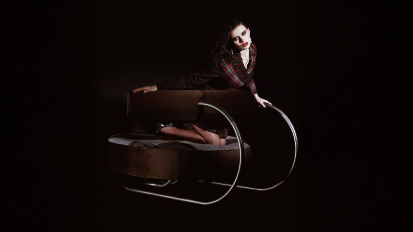 Photograph of a person wearing a tartan-patterned dress posing on a sculptural chair with a stainless steel frame and a curvaceous brown backrest.