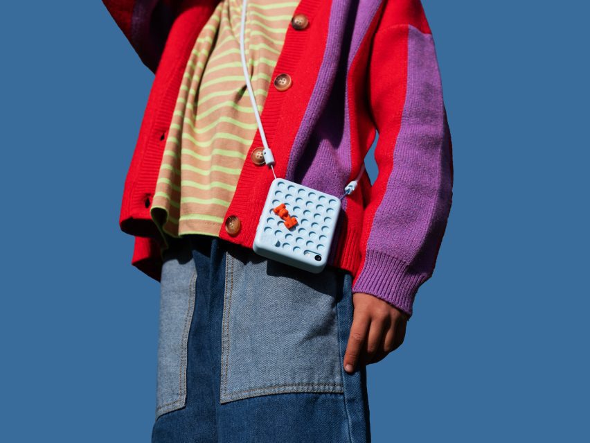 Close-up photo of a Freckle phone decorated with a boy charm, as worn around a child's neck as they stand in the outdoors
