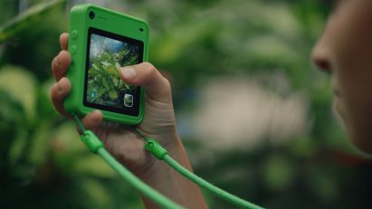Close-up photo of the screen of a Freckle phone in a forest setting while a child snaps a photo of some foliage
