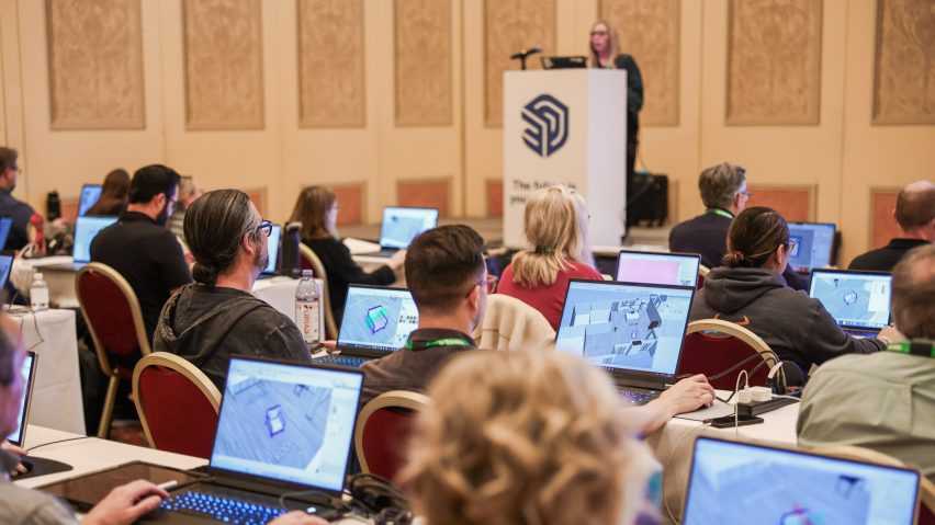 Attendees sitting at tables using laptops during a SketchUp workshop, with a presenter standing at a lectern at the front of the room