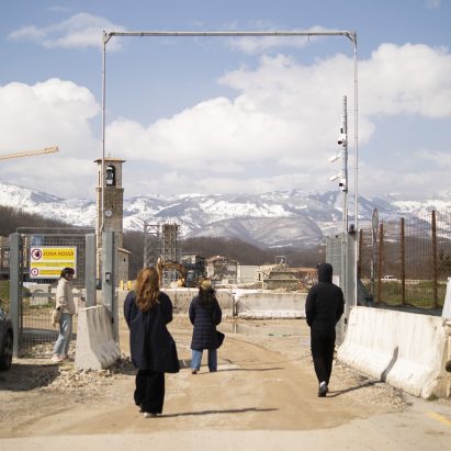 People walking into a construction site at the foot of some snow-capped mountains