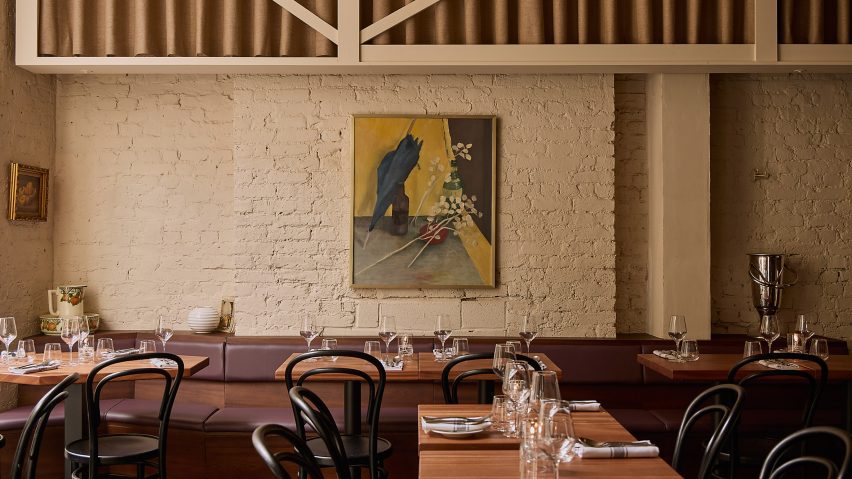 Photograph of the restaurant interior with exposed brickwork, wooden tables and dark banquette seating. There is a large piece of artwork on the wall.