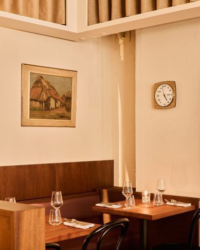 Photograph of a small corner of the restaurant with cream walls, dark-wood banquette seating and wooden tables