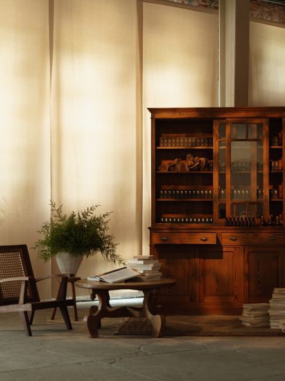 A wooden cabinet displays fragrance bottles and ingredients beside books and plants