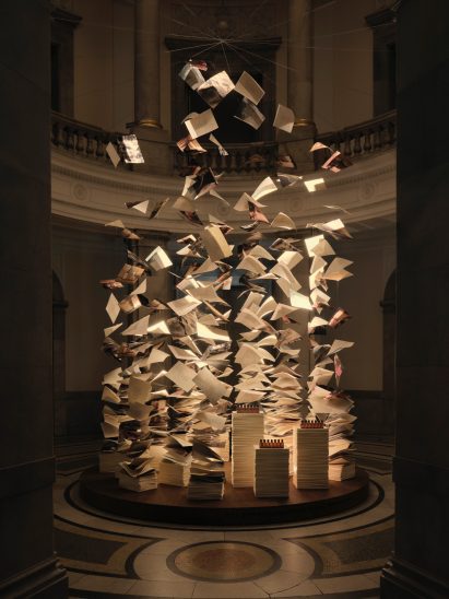 Suspended paper sheets and books forming an installation inside a grand museum interior