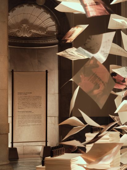 Printed paper sheets and fragrance bottles suspended beside a museum display
