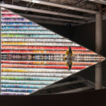 A triangular bookshelf displays rows of colourful books above a circular mirror