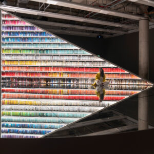 A triangular bookshelf displays rows of colourful books above a circular mirror