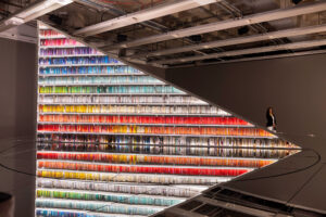 A triangular bookshelf displays rows of colourful books above a circular mirror