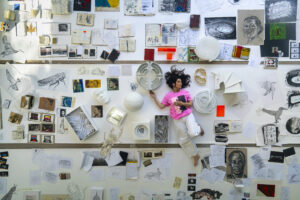 Es Devlin lying on the floor surrounded by drawings, photographs, sketches, models and other creative materials